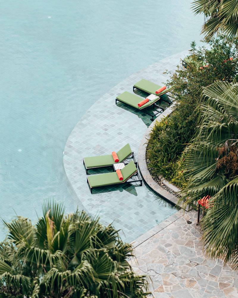Resort pool with loungers on a shallow ledge, palm trees, seen from above